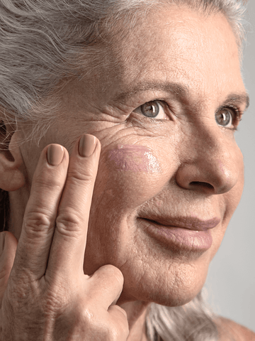 Older woman using Calming Herbal Repair Concentrate Serum Balm on cheeks